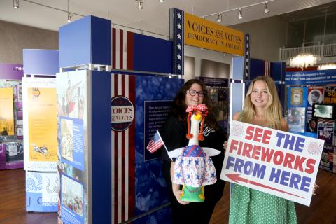 Hart County Chamber of Commerce President and CEO Amanda Brown (left) holding "Nancy Honk," the patriotic porch goose, and Aeva Looney (right), an intern with the Chamber/Hartwell Main Street through the University of Georgia's Archway Program, stand in front of the Smithsonian Exhibit inside the Arts Center of Hartwell Wednesday morning. The pair is advertising a variety of the Pre-4th festivities that will take place alongside the Hartwell Service League's Pre-4th Celebration. Photo by Rose Scoggins. 