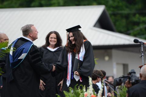 Hart County High School art teacher Amanda Ayers (center) smiles proudly as she watches her daughter, Isabella Ayers (right) receive her diploma from principal Kevin Gaines (left) during Friday's graduation ceremony in Herndon Stadium. Ayers was one of over 240 graduates to receive her diploma during the ceremony. Due to a threat of rain, the event was moved to 6 p.m. from its original time of 8 p.m., and graduates were able to have a rain-free ceremony.  Photo by Benjamin London.