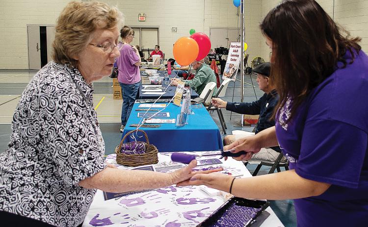 Sunshot by Karen Sokol — Carolyn Mullenix, left, has her hand painted purple by Isabel Bocanegra, right, to take the Purple Pledge with the Northeast Georgia Council on Domestic Violence for Domestic Awareness Month at the Hartwell Helps EXPO on Oct. 5.