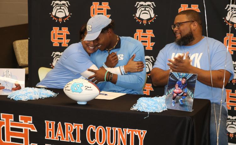 Sunshot by Grayson Williams — Kristi Rucker, left, hugs her son Kaimon Rucker, center, as his father, Kendall Rucker claps during Kaimon’s signing day ceremony on Dec. 18. Kaimon will play college football at the UNiversity of North Carolina.