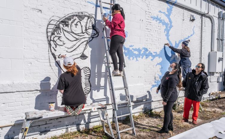 Nora Winkler, from left, Alondra Arevalo, on the ladder, and Katie Eidson, right paint a mural on the rear exterior wall of Little Japan on Depot Street in downtown Hartwell recently as restaurant owners Treena and Tommy Nguyen look on.