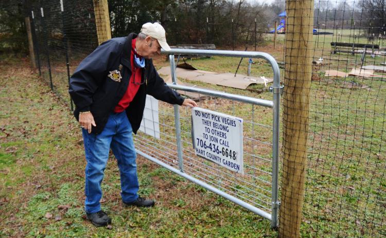 Sunshot by Michael Hall - Frank Spenger adjusts a sign on the gate that was installed as part of a 7-foot-tall deer fence recently constructed around the Hart County Community Garden.