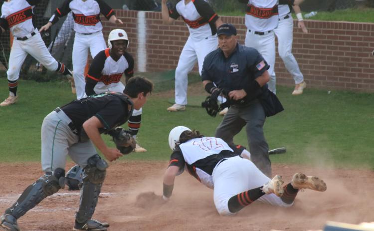Will Dean slides head-first into home plate and beats the tag to add another run in the Diamond Dogs’ late-inning surge to take a 3-1 victory over region rival Franklin County as fellow Bulldogs celebrate in front of him at home on Tuesday, March 30.