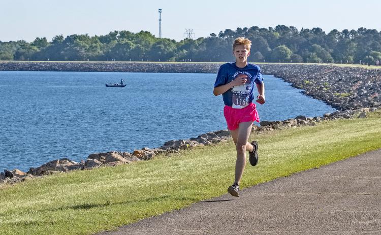 Courtesy of Gwynn Powell - A fisherman goes about his Saturday as normal as Hartwell’s own Zachary Benner, 17, flies past him en route to a first place finish in the 5K with a time of 17:21.