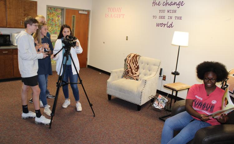 Junior softball player Jakheera Burton, pictured seated right, reads Not Quite Snow White by Ashley Franklin while video production students, pictured left, in the Hart College and Career Academy film a “Books with Bulldogs” episode.