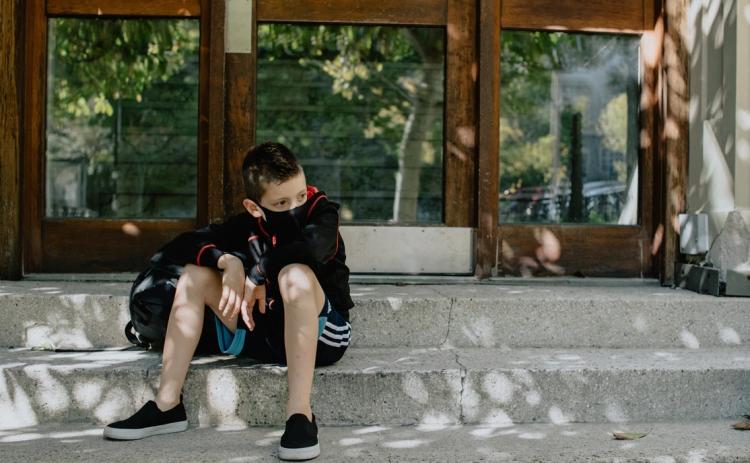 A boy with mask on on the steps waiting for school. Photo credit: Kelly Sikkema