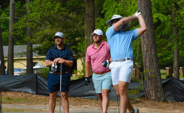 Pictured, John Daniel Gibbs tees off while his partner, Winston Gibbs (left), and Dillon Bowers (middle) watch the ball.