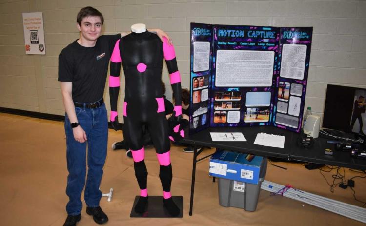 HCHS senior Stanley Maxwell stands alongside the suit that has helped his group for the past four years create 3-D animation.