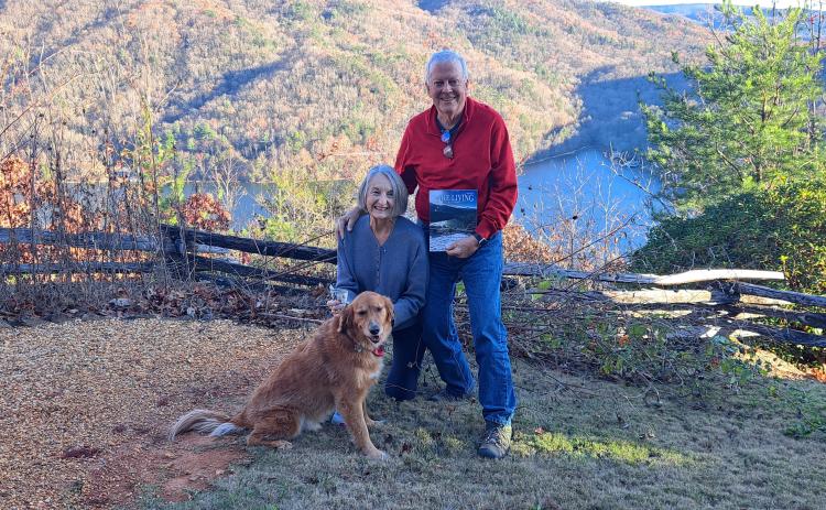 A picture viewing a snowy mountain range and snow-covered fence at Lake Burton taken by Chip Goen of Clayton is now featured on the cover of the Winter 2024 Lake Living magazine. Lin Goen submitted the photograph to the contest. The Goens are pictured here with their dog Charley, the Lake Living magazine cover and $100, with the same backdrop in a different season.