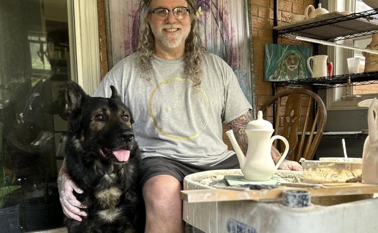 Chad Whitworth, ceramicist and owner of Nevermore Studios, sits at the pottery wheel in his home studio with Judge, a retired k9 german shepherd, by his side. While Whitworth rarely allows anyone else to enter his studio, Judge always keeps Whitworth company during his long hours of throwing on the wheel. (Photo submitted by Whitworth)