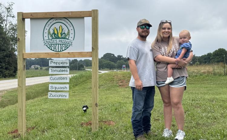 The Saxon family (L-R) Garrett Saxon, Breanna Saxon and Annalee Saxon stand next to the Saxon’s Produce sign located at 8701 Bowman Highway in Dewy Rose. Saxon’s Produce first opened on Memorial Day 2025 and sells double-yolk eggs, pickles and produce. (Photo/Adriana Cascio)