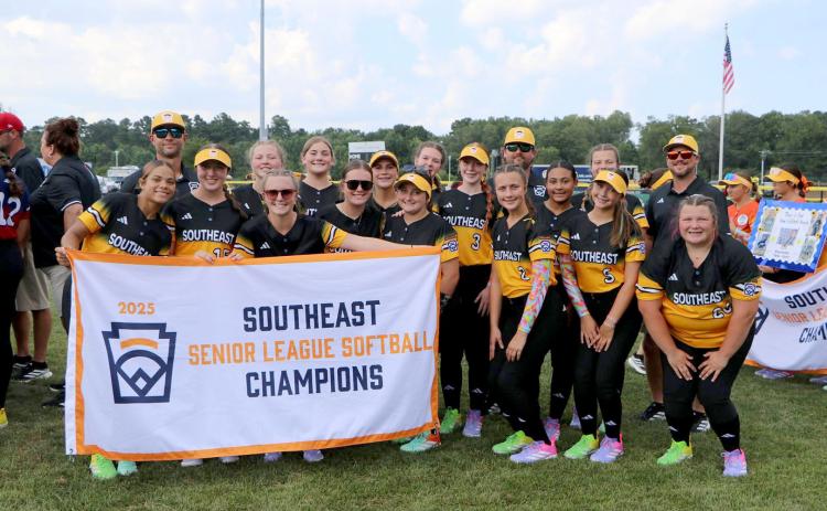 Hart County Senior League Softball team poses with their Southeast Champions banner before a game in the Senior League Softball World Series in Lower Sussex, Delaware. The team consists of Milo Allen, Marlee Bowers, Maggie Bridges, Ky Dubose, Kinsley Duncan, Peyton Jordan, Emory McCollum, Peyton McCollum, Emma Mitchell, Kam Price, Erika Royston, Bella Segars, Chesnee Strickland, EmmaKate White and MaryBeth White. The team is coached by Kyle McCollum, Mason Bowers, Tony Strickland and Head Coach Paul Mitchel