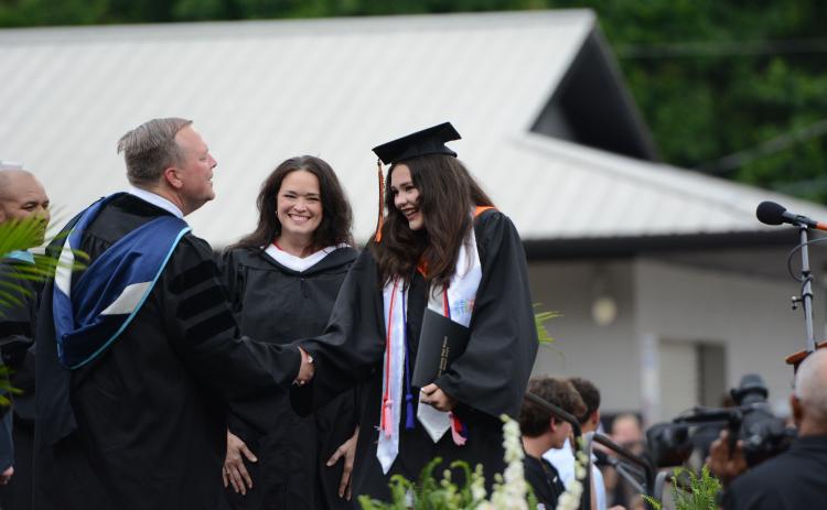 Hart County High School art teacher Amanda Ayers (center) smiles proudly as she watches her daughter, Isabella Ayers (right) receive her diploma from principal Kevin Gaines (left) during Friday's graduation ceremony in Herndon Stadium. Ayers was one of over 240 graduates to receive her diploma during the ceremony. Due to a threat of rain, the event was moved to 6 p.m. from its original time of 8 p.m., and graduates were able to have a rain-free ceremony.  Photo by Benjamin London.