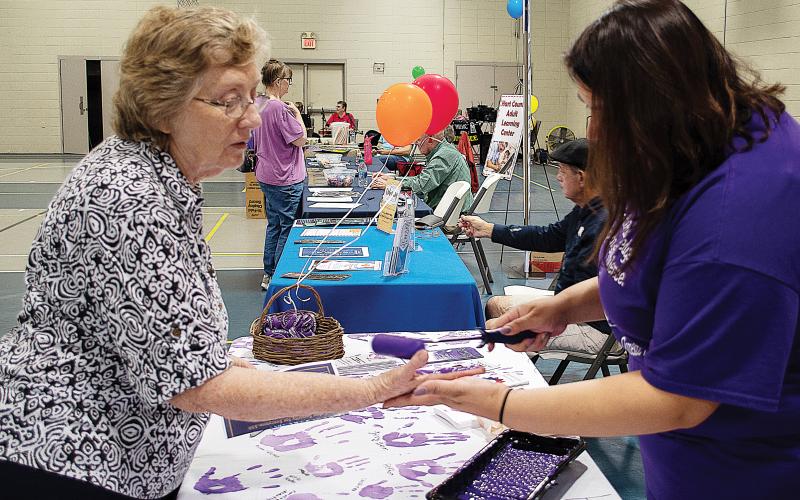 Sunshot by Karen Sokol — Carolyn Mullenix, left, has her hand painted purple by Isabel Bocanegra, right, to take the Purple Pledge with the Northeast Georgia Council on Domestic Violence for Domestic Awareness Month at the Hartwell Helps EXPO on Oct. 5.