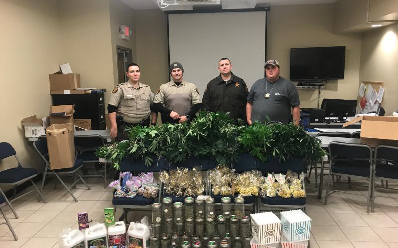 Sunshot from file — Hart County Sheriff’s deputies Luke Bennett, Michael Davis, Jared Tollinson and Capt. Kevin White pose for a photo with an array of marijuana plants and marijuana-related products allegedly being grown and manufactured at a house on Lanier Street in Hartwell.
