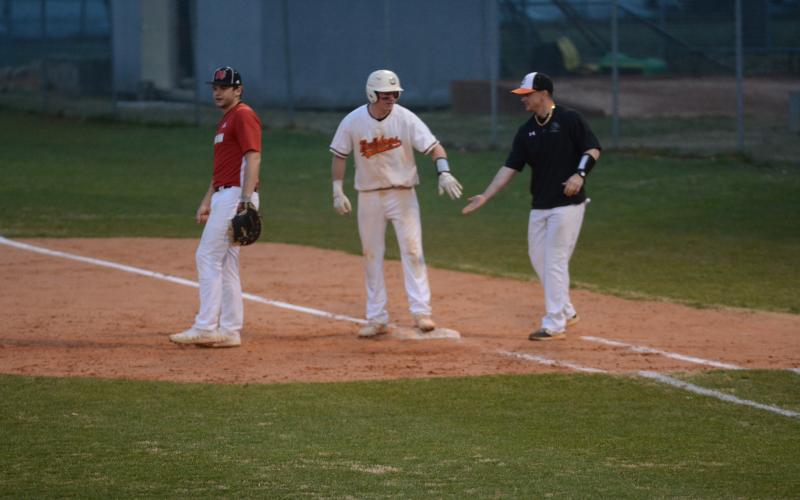Luke Lee, left, is congratulated by coach Hunter Barton, at first base after Lee’s line drive that drove in a run to take the lead against Morgan County on Monday at Saye Field. 