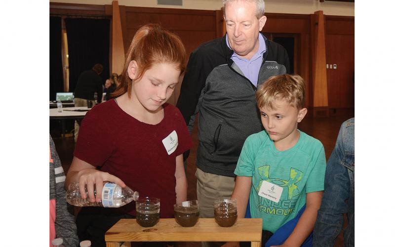 Mackenzie Marlow, left, pours water into soil to see how well it filters through as Ron Wright, of the Golf Course Superintendents Association of America, center, and Chase Moriarty look on at Cateechee in November during the first, First Green field trip at the golf club and conference center.