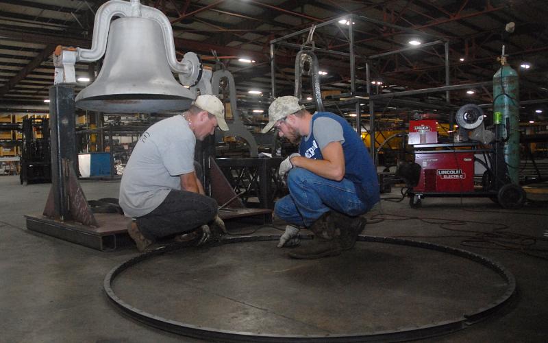 Sunshot from file — Fabritex metal fabricators Martin Neal, left, and Jon Grubbs, right, layout the wheel at Fabritex in 2018 that is now part of a mechanisim used to ring the Victory Bell at Hart County High School. The company refurbished the bell and renewed a longstanding tradition for Hart County Schools, one of many ways Fabritex partners with local schools. 