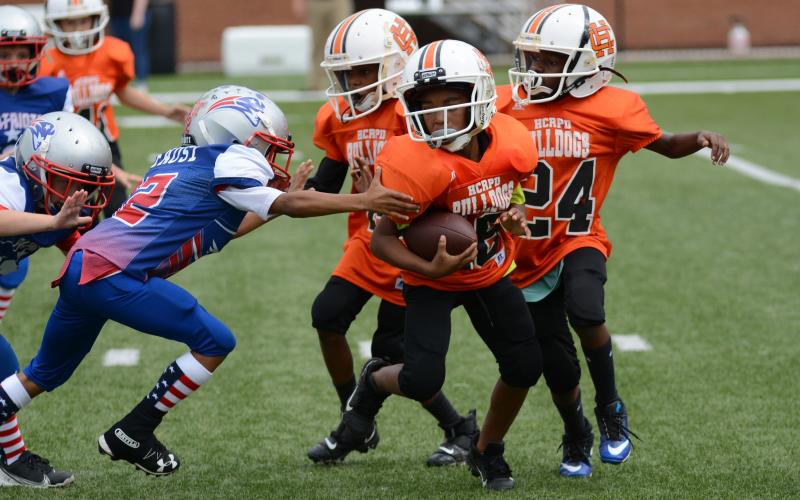 Cason Williams, 8U quarterback, runs with the football as Rexdriquez Hill, right, and Christian Marshall, to the left of Williams, look for Patriots to block.