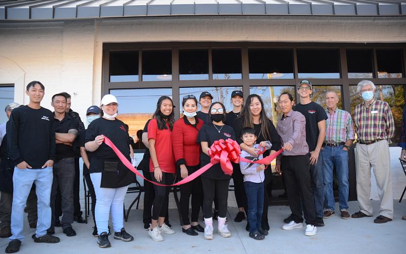 Chance Nguyen holds a pair of giant scissors to cut the ribbon held by his sister Jaslene Nguyen, to the left of Chance, on Monday, Nov. 23, for Little Japan, which is owned by their parents Treena, behind Chance, and Tommy Nguyen. 