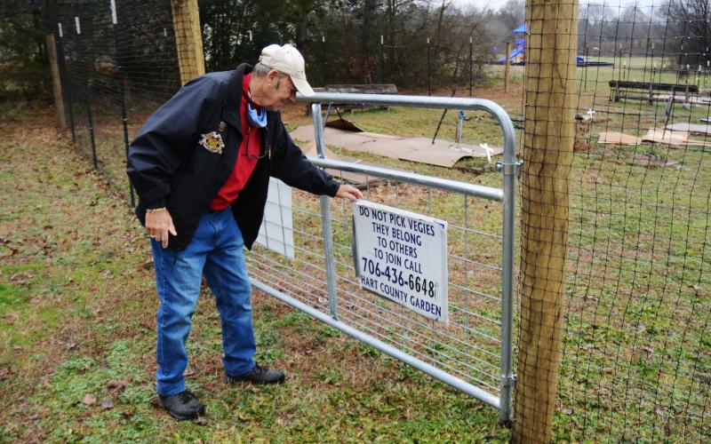 Sunshot by Michael Hall - Frank Spenger adjusts a sign on the gate that was installed as part of a 7-foot-tall deer fence recently constructed around the Hart County Community Garden.