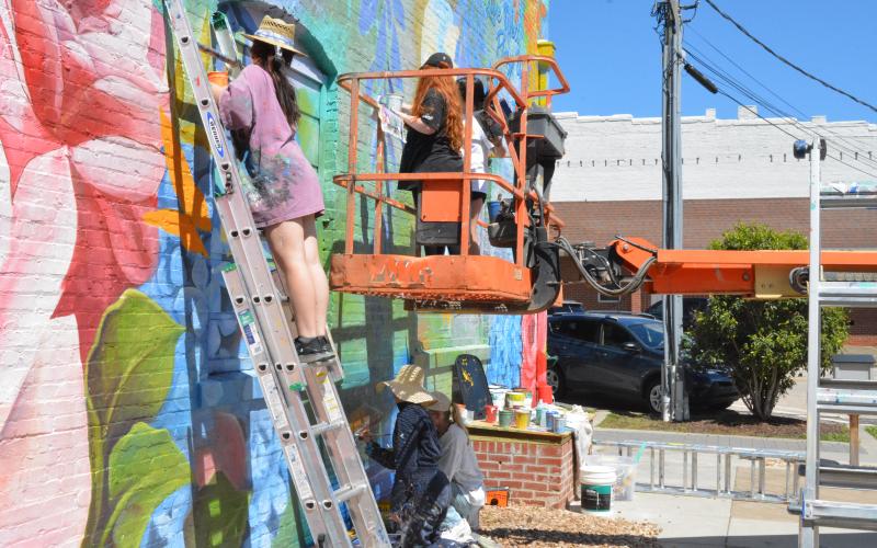 Jennifer Pham works on a butterfly on the mural on a ladder. Nora Winkler, left, and Alondra Arevalo, right, work high on the lift while Katie Eidson, left, and Gabriel Poteet, right, work on the swing closer to the ground.