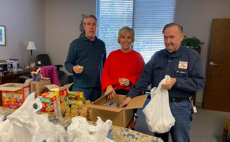 Hart EMC Director of Public Relations Angie Brown, center, recently visited the Hart Partners, Inc. offices in downtown Hartwell to see the Food for Kids Friday Backpack Program in action. Community volunteers Greg Blatt, left, and John Mead, add supplemental food items to bags.